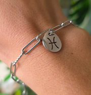 Bracelet argenté en acier inoxydable avec pendentif astrologique des Poissons, création Therapietra, porté au poignet.