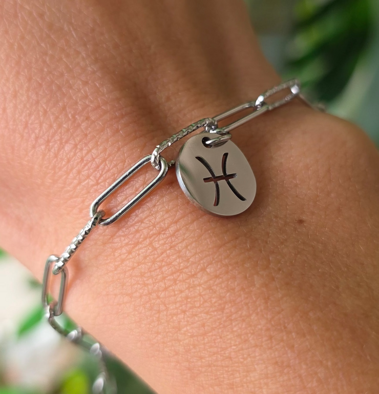 Bracelet argenté en acier inoxydable avec pendentif astrologique des Poissons, création Therapietra, porté au poignet.