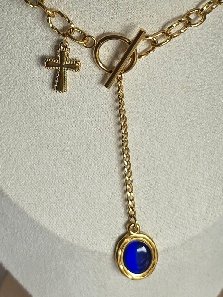 Collier Azura Aurea – bijou doré orné d’une croix et d’une pierre bleue, symbole de foi, noblesse et lumière intérieure.