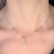 Collier Lyria signé Therapietra, bijou en acier inoxydable doré avec pierre d’améthyste et lettre rose. Symbole de paix intérieure et d’amour doux.