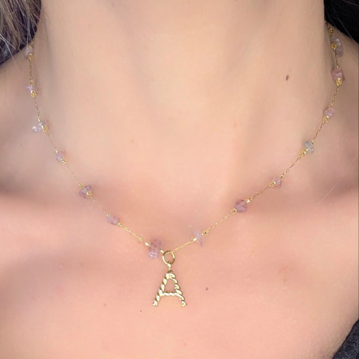 Collier Lyria signé Therapietra, bijou en acier inoxydable doré avec pierre d’améthyste et lettre rose. Symbole de paix intérieure et d’amour doux.